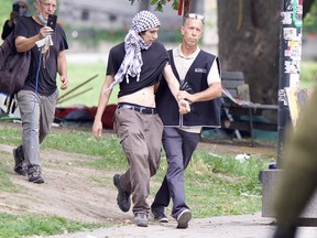 A man escorts a protester. Another man follows, recording with his phone.