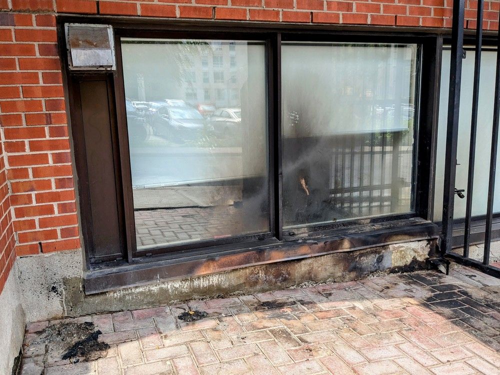 A ground-level window has burn marks on the glass and on the brick floor in front of it