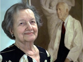 Profile shot of a smiling woman with the portrait of a man behind her.