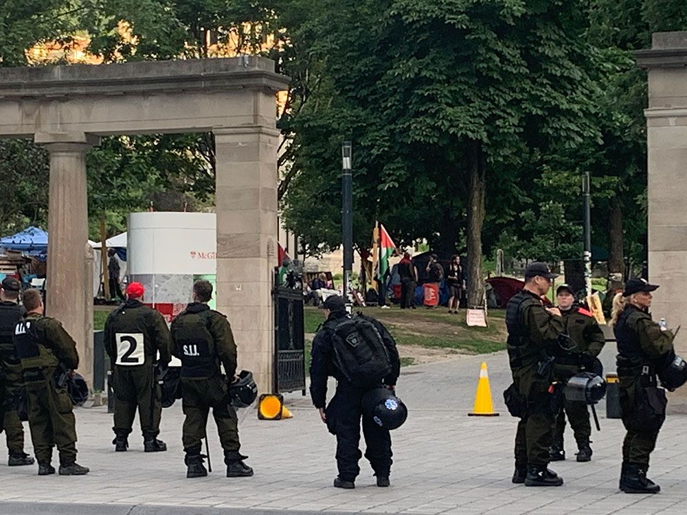 Police stand at university gates. A Palestinian flag can be seen on the other side of the gates.