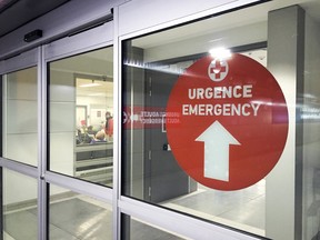 An emergency sign is next to a sliding door at a hospital entrance.