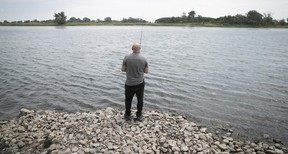 A man fishing on a rocky shore, seen from behind.