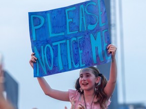 A girl holds a handmade sign that says Please Notice Me