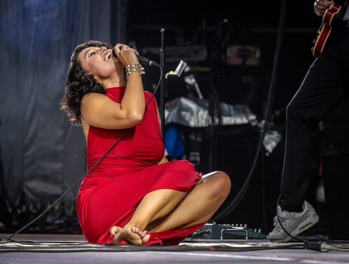 Raye seated bareoot on the stage as she sings
