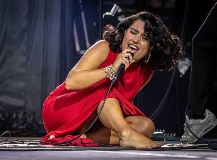 Raye seated bareoot on the stage as she sings