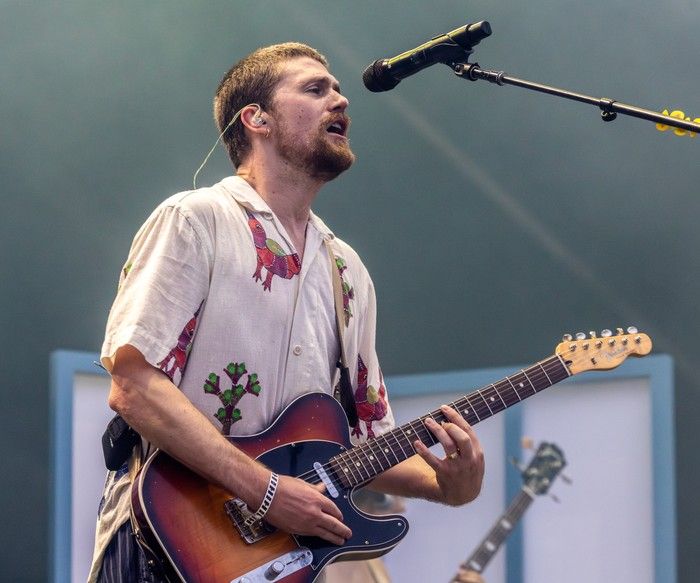 A man sings into a microphone while playing the electric guitar