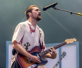 A man sings into a microphone while playing the electric guitar