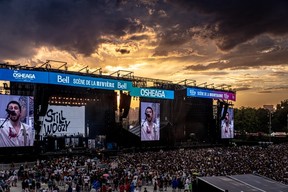 Wide view of a festival stage at sunset with a man singing on the big screens