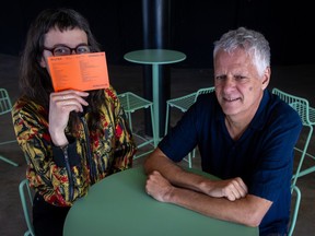 Two people sit at a table, one holding a card in front of her face