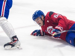 David Reinbacher, wearing a red Canadiens practice jersey, lays on the ice