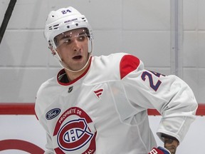 Logan Mailloux, wearing number 24 in a Canadiens white practice jersey, looks over his shoulder on the ice
