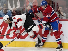 A Canadiens player stands behind a Devils player falling forward to the ice along the boards