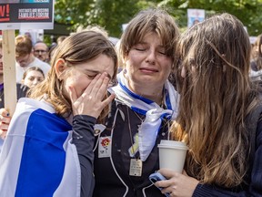 Several women hug and cry, one draped in an Israeli flag