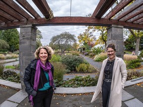 Two women stand outside under a pergola with gardens in the background