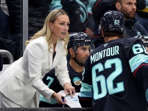 Jessica Campbell, wearing a suit, leans over and talks to a Seattle Kraken player from behind the bench