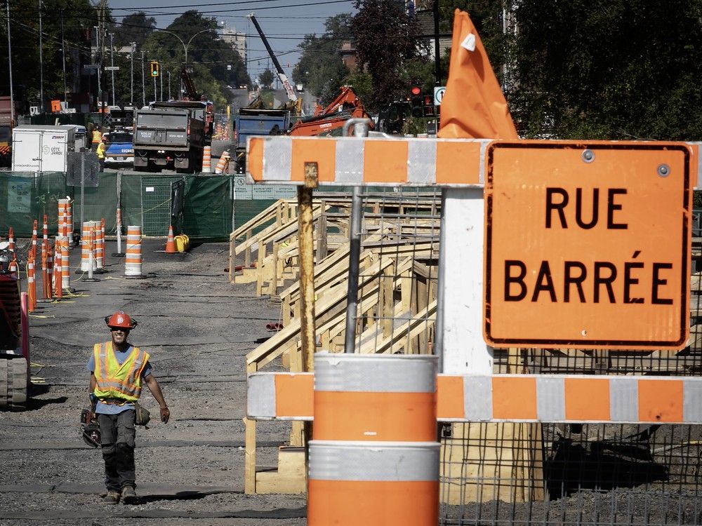 a construction worker walks down a closed street with orange cones and a "rue barrée" sign in the foreground