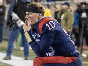 Davis Alexander holds his chin in his hand while kneeling on the sideline of a football field