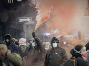 A masked protester holds up a smoke torch
