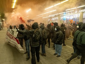 A group of masked protesters on a covered street filled with smoke
