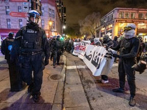 A street has riot police facing protesters holding up banners at night