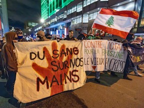 At a protest at night on a downtown street, banners reading 'Du sang sur nos mains' and 'Contre l'OTAN, pour la Palestine le vieux (illegible) criss'