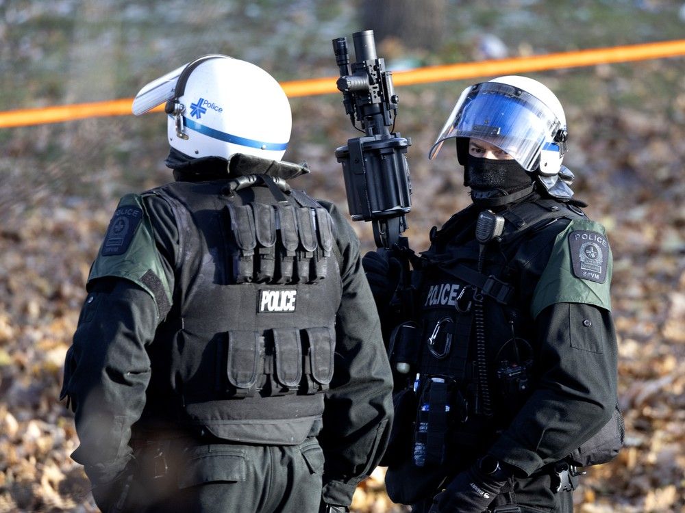  montreal police stand guard with a standard launcher used for tear gas or rubber bullets as  a portion of the notre-dame st. homeless encampment is cleared inside the morgan park fenced boundaries in montreal, dec. 2, 2024.