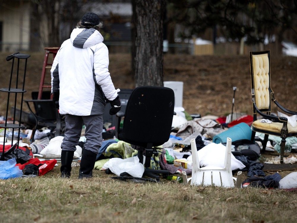 a man is seen from behind as he looks at abandoned items strewn around an encampment.