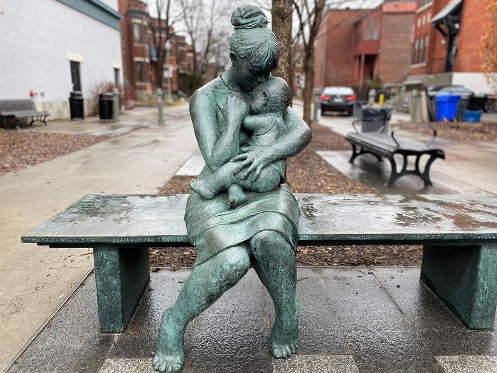 a bronze sculpture depicts a woman holding a baby, sitting on a bench.
