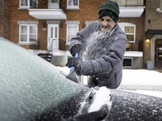 A older man in a toque scrapes ice off his windshield.