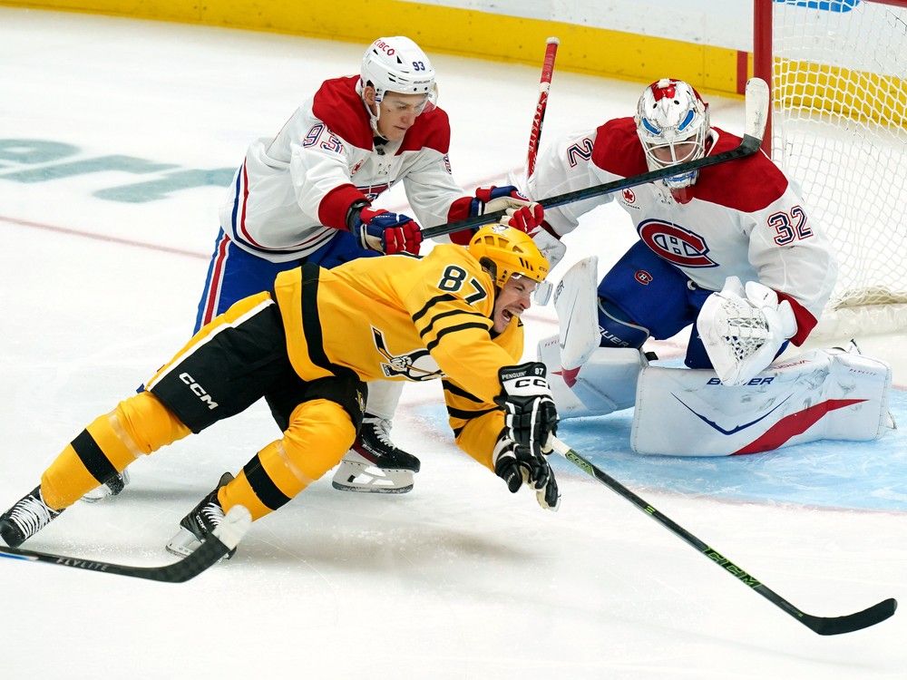 Hockey player diving in front of net to get puck while goalie watches