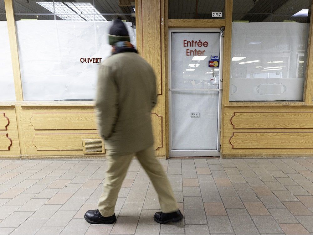A man walks by a bakery's windows covered in paper after it closed shop.