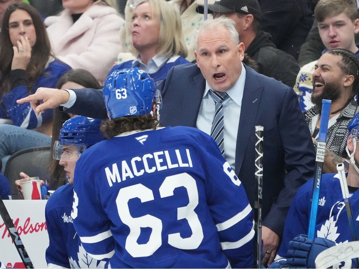 Leafs head coach Craig Berube leans over players on his bench to talk to forward Matias Maccelli on the ice.