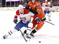 Hockey player fends off an opponent that is draped over him.