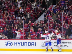Two Canadiens players celebrate on the ice while a crowd of people mostly in Canadiens jerseys cheers in the stands