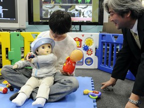 Tokyo University professor Yasuo Kuniyoshi (R) looks on as Japanese post-graduate student Kosuke Nakamura plays with the robot baby named Noby.