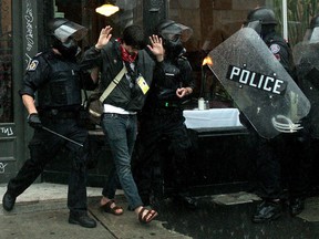 A journalist with visible credentials is arrested by riot police as rain pours down at the conclusion of the G20 summit