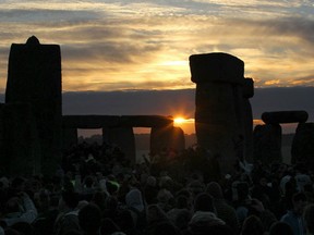 Revellers watch as the midsummer sun rises just after dawn over the megalithic monument of Stonehenge.