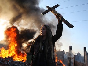 BASILDON, ENGLAND - OCTOBER 19:  An activist holds up a crucifix as a barricade burns during evictions from Dale Farm travellers camp on October 19, 2011 near Basildon, England. Travellers have fought for 10 years to stay on the former scrap yard site. The local authorities have been given the go-ahead to proceed with the eviction of illegal dwellings after rulings by the Court of Appeal.  (Photo by Peter Macdiarmid/Getty Images)