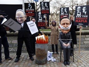 A protester wearing a mask depicting Rupert Murdoch, left, pretends to burn a mock Leveson Report as a protester wearing a mask of British Prime Minister David Cameron sits bound and gagged. (JUSTIN TALLISJUSTIN TALLIS/AFP/Getty Images)