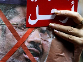 An Egyptian protester holds anti-President Mohammed Morsi poster and a red card with Arabic word "Leave" during a protest in Cairo, Egypt, Saturday, June 29, 2013.