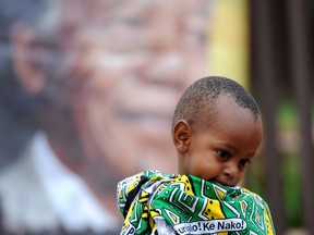 A child draped in a cloth in the African National Congress colors, stands outside the former home, now museum, of former South African president Nelson Mandela, portrait in background,  in Soweto, South Africa, Friday, Dec. 6, 2013. Mandela passed away Thursday night after a long illness. He was 95. As word of Mandela's death spread, current and former presidents, athletes and entertainers, and people around the world spoke about the life and legacy of the former South African leader. (AP Photo)