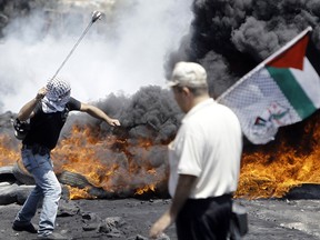 A Palestinian protester  hurls rocks at Israeli security forces as man walks past with a Palestinian flag during clashes following a protest in the village of Kfar Qaddum, near the northern city of Nablus, in the occupied West Bank on August 1, 2014.