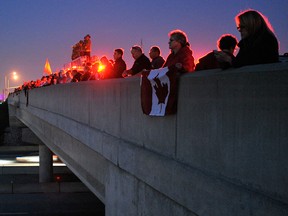The red flashing lights of a fire truck illuminate the hundreds lining a bridge over highway 407 in Mississauga as the motorcade carrying the remains of Cpl. Nathan Cirillo pass through, Oct. 24, 2014.