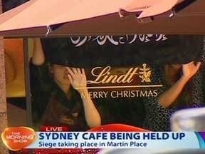 This image taken from video shows people holding up what appeared to be a black flag with white Arabic writing on it, inside a cafe in Sydney, Australia Monday, Dec. 15, 2014.  Australia's largest city on Monday, where several people could be seen through a window with their hands held in the air. (AP Photo/Channel 7 via AP Video) AUSTRALIA OUT