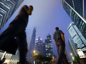 Pedestrians walk past commercial buildings including the Shanghai Tower, center left, under construction at night in the Lujiazui district of Shanghai, China, on Friday, June 28, 2013. China's expansion probably slowed for a second straight quarter, based on the median estimate in a Bloomberg News analyst survey, after export growth collapsed and Premier Li Keqiang reined in record credit expansion to contain shadow-banking risks. Photographer: Tomohiro Ohsumi/Bloomberg