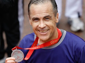 Mark Carney, Governor of the Bank of England holds up his medal after completing the 35th London Marathon in 2015.