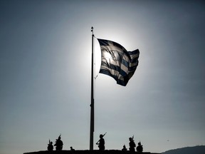 An army contingent stands below a fluttering Greek flag after a hoisting ceremony at the Acropolis hill in Athens, Greece