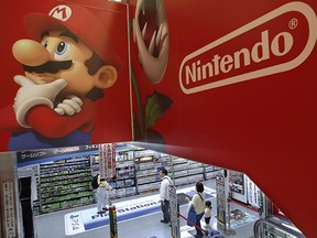 Shoppers walk under the logo of Nintendo and Super Mario characters at an electronics store in Tokyo Wednesday, May 7, 2014. Nintendo Co. sank to a loss for the fiscal year ended March as sales of its Wii U game machine continued to lag, but the Japanese manufacturer of Pokemon and Super Mario games promised Wednesday to return to profit this year. (AP Photo/Shizuo Kambayashi) ORG XMIT: XKAN103