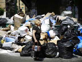 A Lebanese woman holds her nose from the smell as she passes by a pile of garbage on a street in Beirut, Lebanon, Tuesday, July 21, 2015.