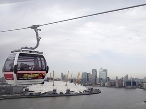 An Emirates Air Line cable car carries passengers across the River Thames, in front of the London O2 Arena, left, and the Canary Wharf business and financial district in London.